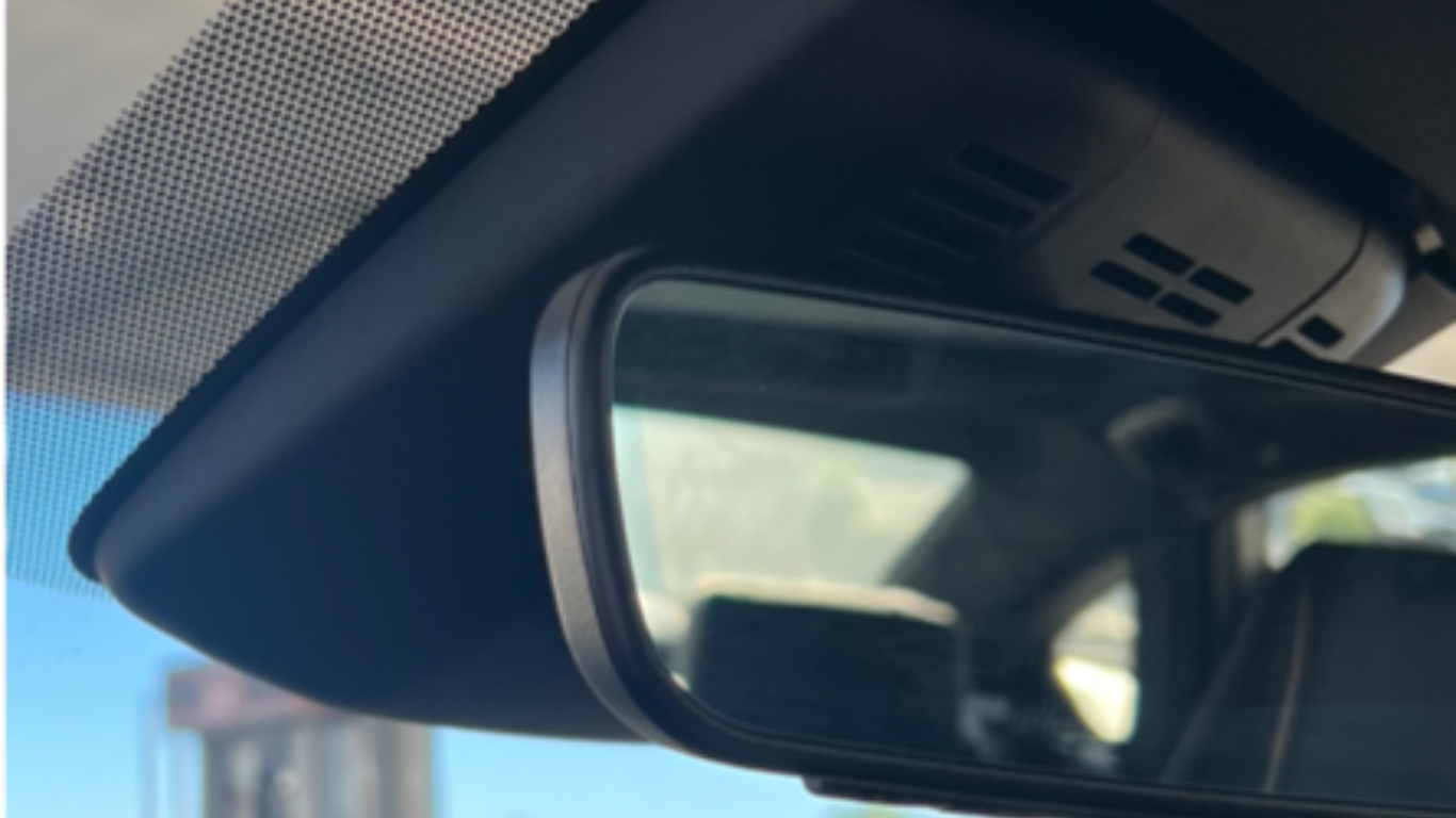 A close-up view of a car's rearview mirror and windshield area, emphasizing the importance of durable retractors for securely supporting an Eclipse Sun Shade.